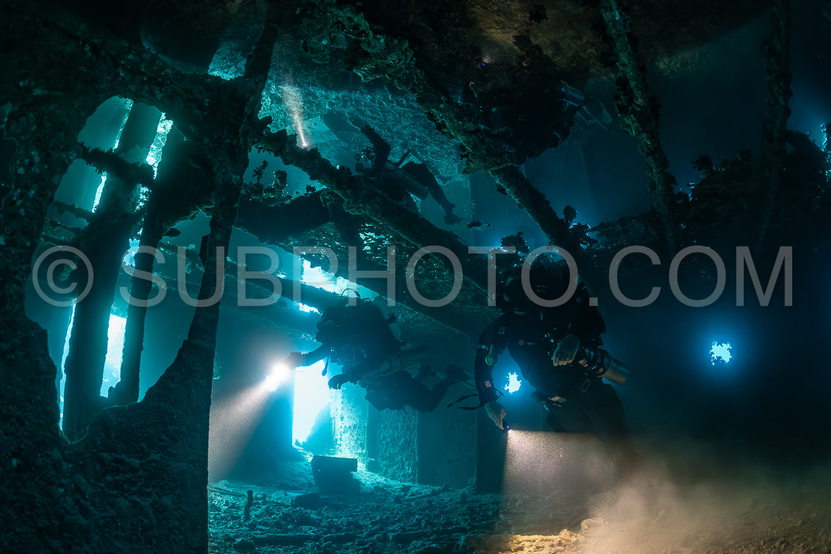 A diver- silhouetted against the blue light filtering through the wreckage- explores the interior of a sunken ship in the Red Sea.