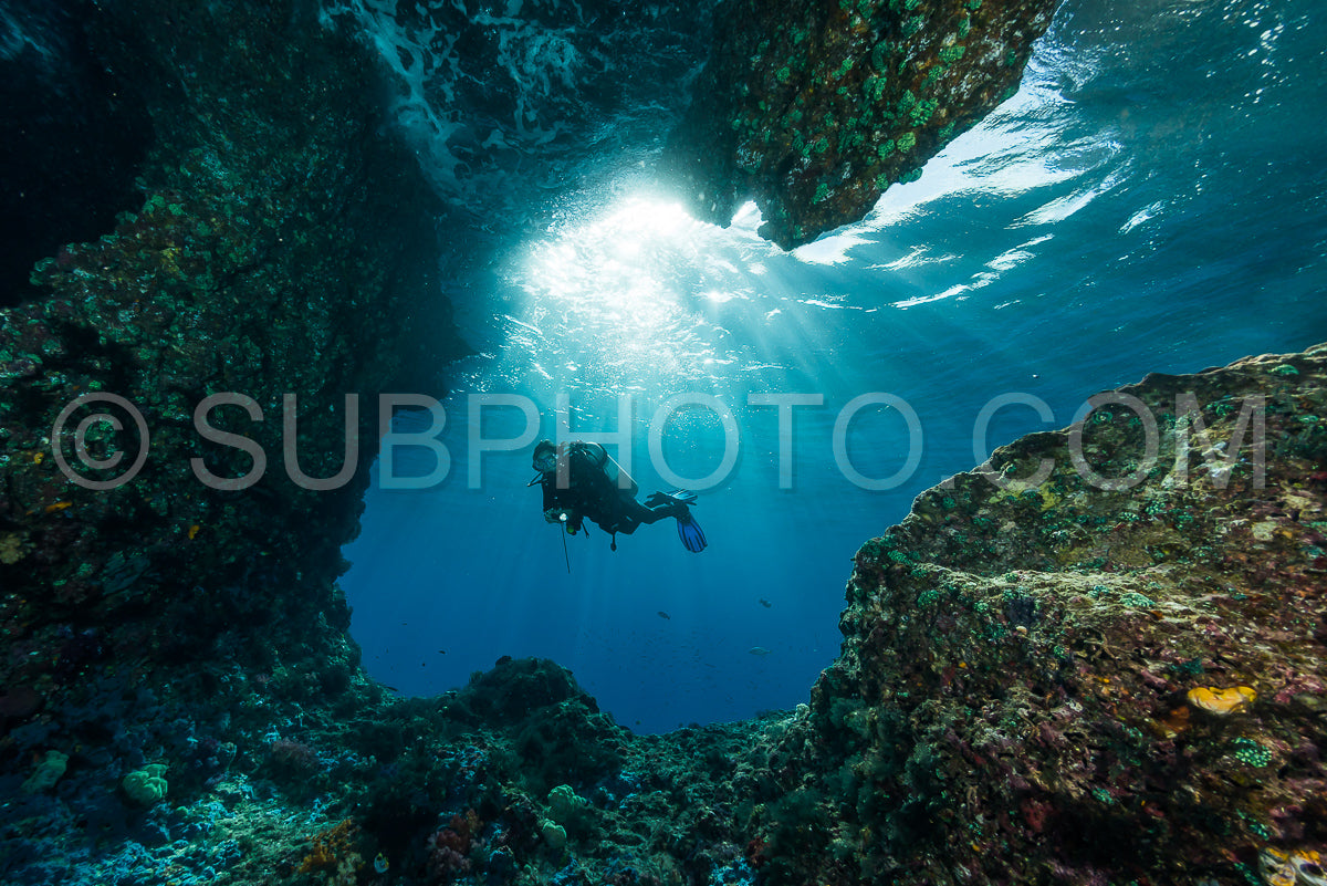 Photo de femme plongeant sous l'eau à l'entrée d'une grotte avec des rayons de soleil