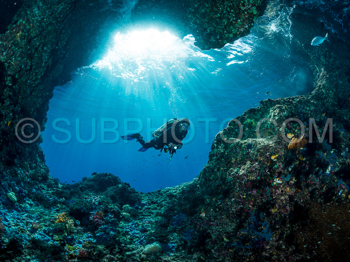 Photo de femme plongeant sous l'eau à l'entrée d'une grotte avec des rayons de soleil