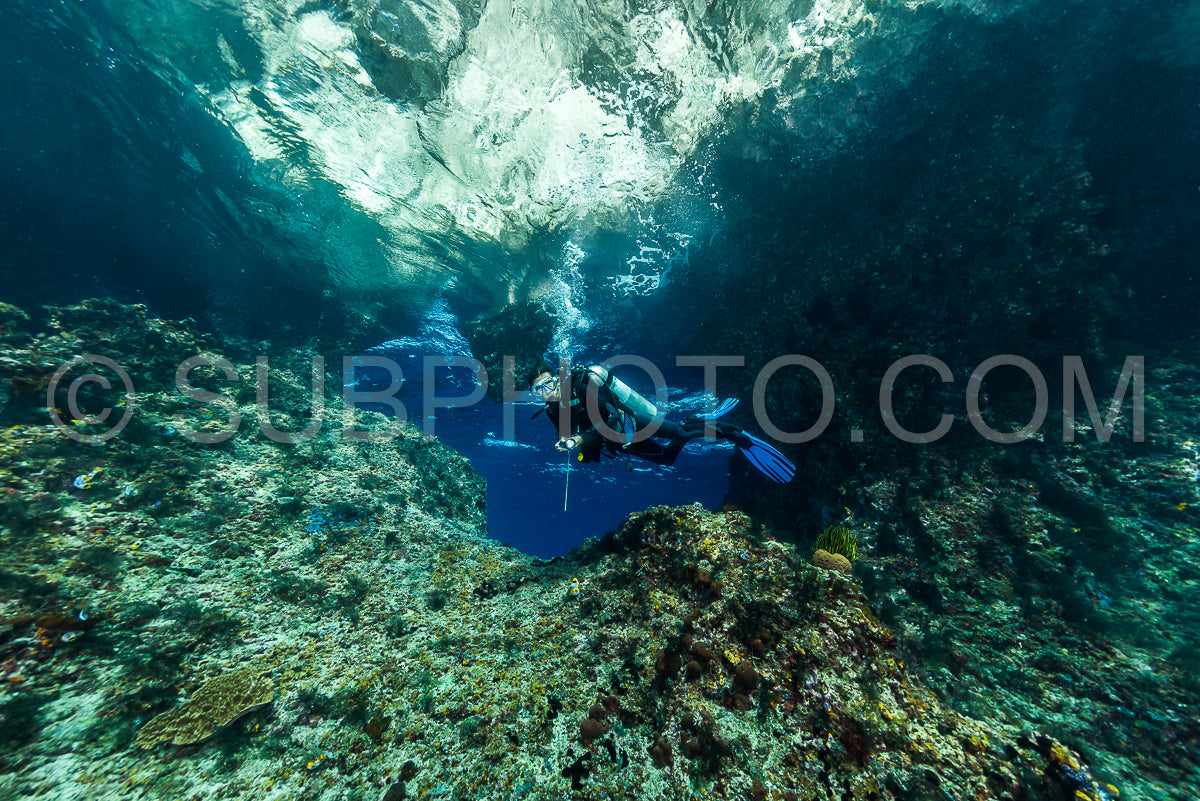 Photo de femme plongeant sous l'eau à l'entrée d'une grotte avec des rayons de soleil
