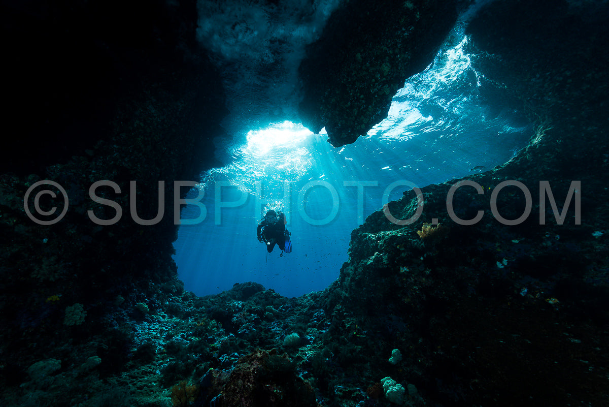 Photo de femme plongeant sous l'eau à l'entrée d'une grotte avec des rayons de soleil