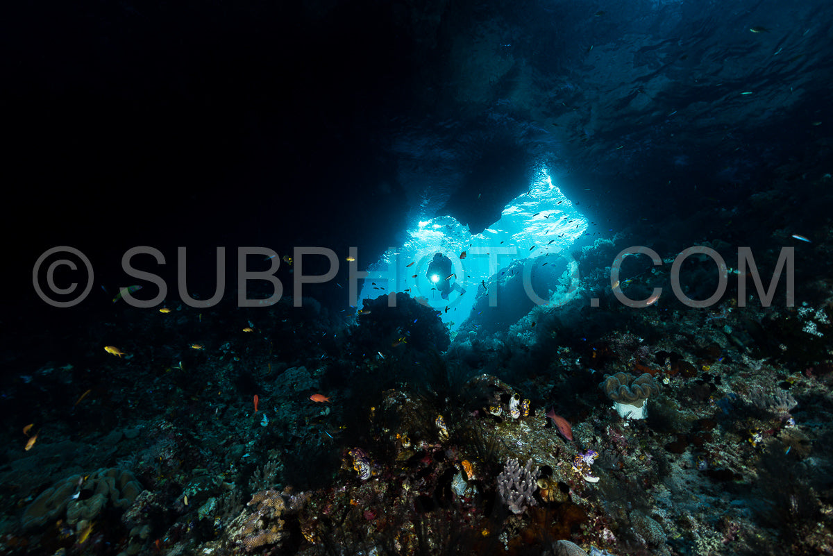 Photo de femme plongeant sous l'eau à l'entrée d'une grotte avec des rayons de soleil
